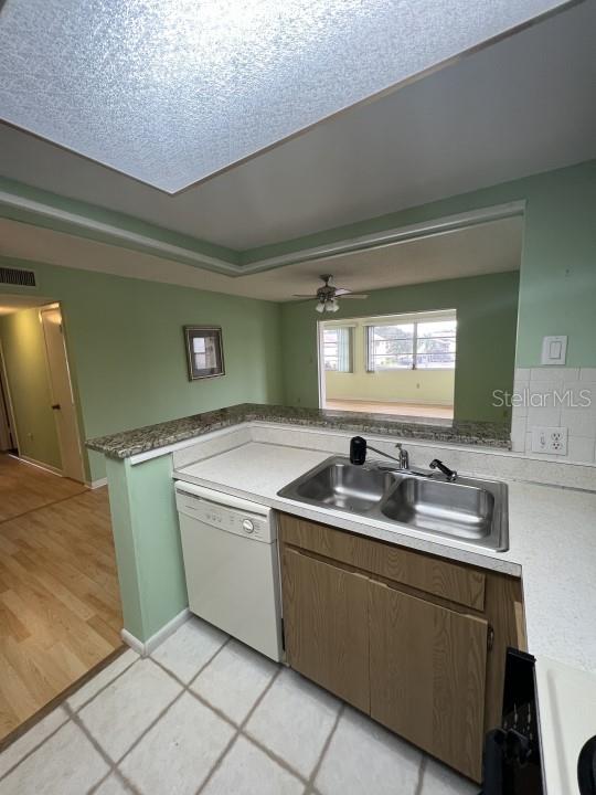 kitchen featuring kitchen peninsula, ceiling fan, dishwasher, light tile patterned flooring, and sink