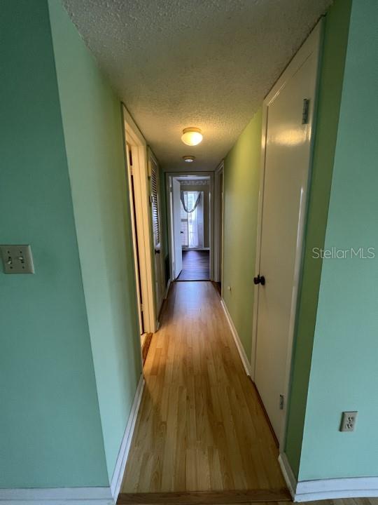 corridor with a textured ceiling and light wood-type flooring