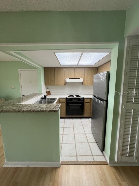 kitchen featuring sink, light wood-type flooring, electric range, kitchen peninsula, and stainless steel fridge