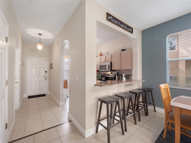 kitchen with a wealth of natural light, light brown cabinetry, a kitchen bar, hanging light fixtures, and stainless steel appliances