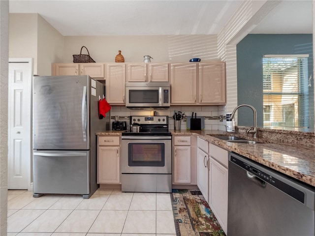 kitchen with sink, stainless steel appliances, tasteful backsplash, light stone counters, and light tile patterned flooring