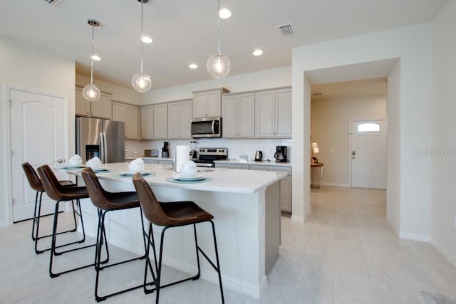 kitchen featuring decorative light fixtures, a kitchen breakfast bar, stainless steel appliances, and a kitchen island with sink