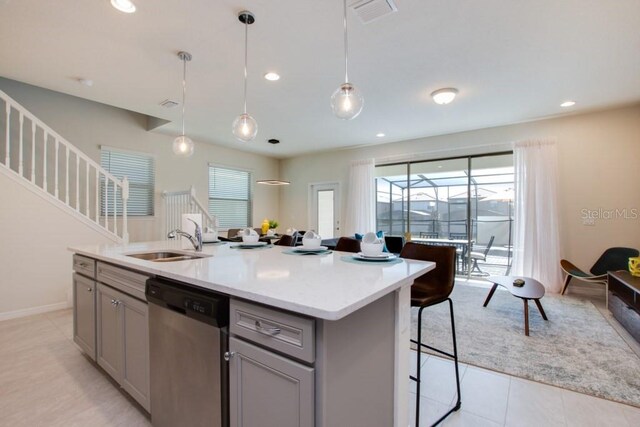 kitchen with stainless steel dishwasher, decorative light fixtures, light tile flooring, gray cabinetry, and a kitchen island with sink