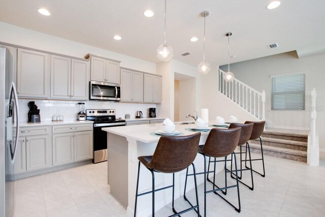 kitchen featuring an island with sink, stainless steel appliances, light tile flooring, a breakfast bar, and hanging light fixtures