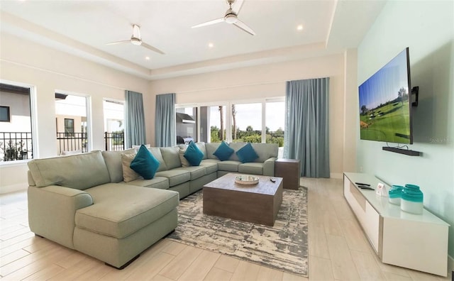 living room with a raised ceiling, ceiling fan, and light wood-type flooring