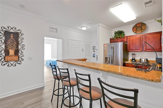 kitchen featuring light hardwood / wood-style flooring, stainless steel refrigerator with ice dispenser, light stone counters, a textured ceiling, and a kitchen breakfast bar