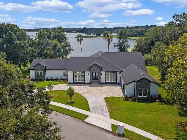 view of front of home featuring decorative driveway, stone siding, a front yard, and a water view