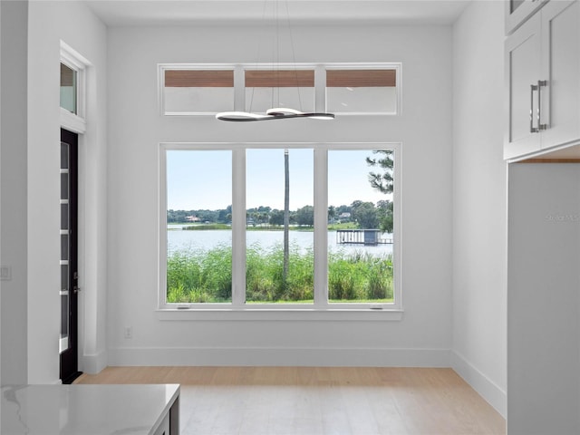 unfurnished dining area with baseboards, a water view, and light wood-style floors