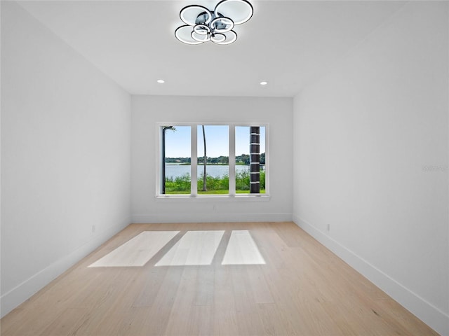 empty room with baseboards, light wood-style flooring, recessed lighting, a water view, and a notable chandelier