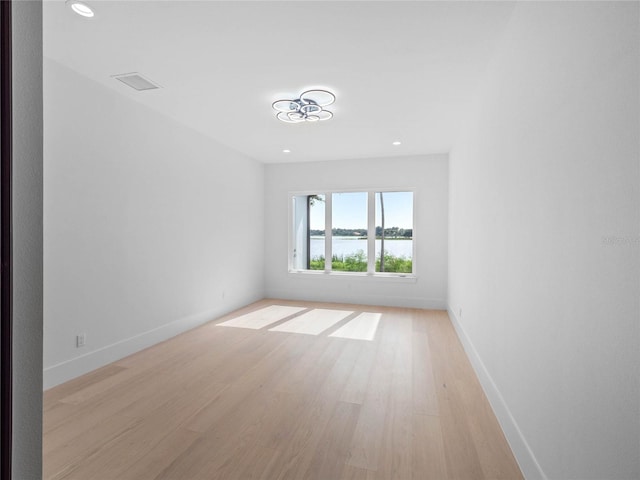 empty room with visible vents, a water view, recessed lighting, light wood finished floors, and baseboards