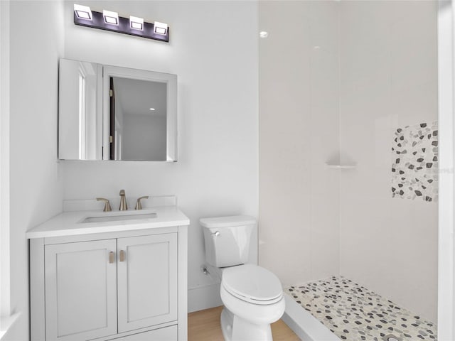 bathroom with toilet, tiled shower, vanity, and wood finished floors