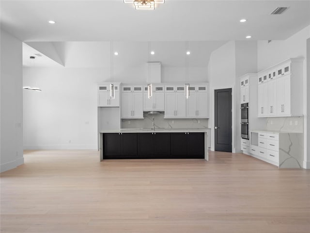 kitchen featuring a large island with sink, decorative backsplash, white cabinets, and light hardwood / wood-style floors