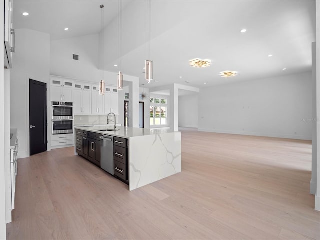 kitchen with a sink, appliances with stainless steel finishes, light wood-style floors, white cabinetry, and a kitchen island with sink