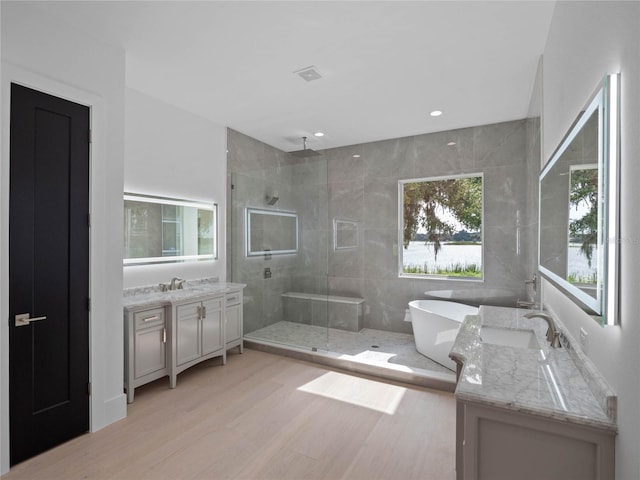 full bath with two vanities, a stall shower, a sink, wood finished floors, and a freestanding bath