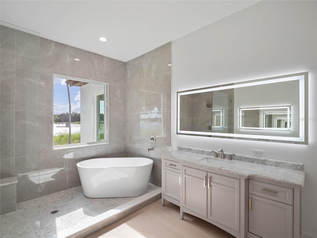 bathroom with separate shower and tub, vanity, and tile walls