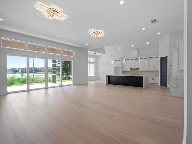 unfurnished living room with light wood finished floors, visible vents, recessed lighting, and a towering ceiling