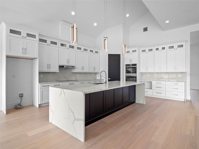 kitchen featuring a spacious island, visible vents, light wood-type flooring, white cabinets, and a sink