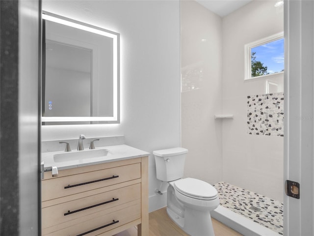 bathroom with tiled shower, toilet, vanity, and wood finished floors