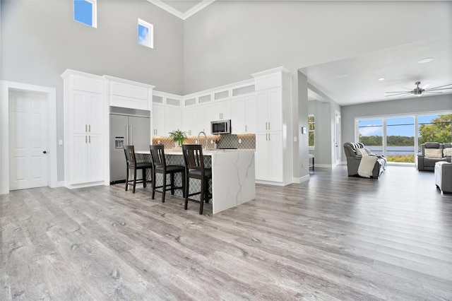 kitchen featuring appliances with stainless steel finishes, white cabinets, light wood-type flooring, and tasteful backsplash