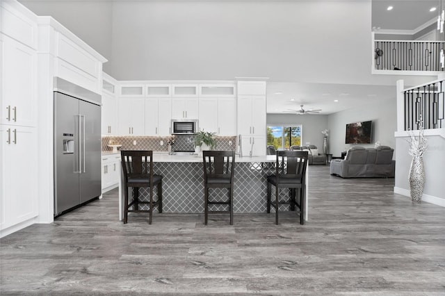 kitchen featuring a center island with sink, appliances with stainless steel finishes, white cabinetry, ceiling fan, and hardwood / wood-style floors