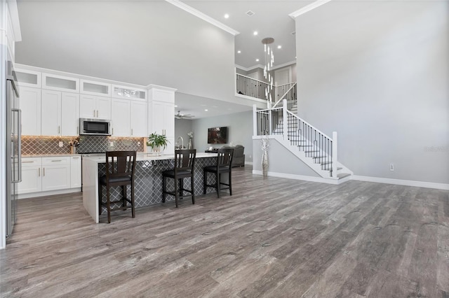 kitchen with white cabinetry, a center island with sink, ornamental molding, dark hardwood / wood-style flooring, and a breakfast bar area