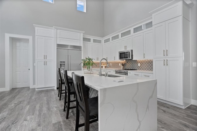 kitchen with light stone counters, a kitchen island with sink, high quality appliances, a high ceiling, and light wood-type flooring