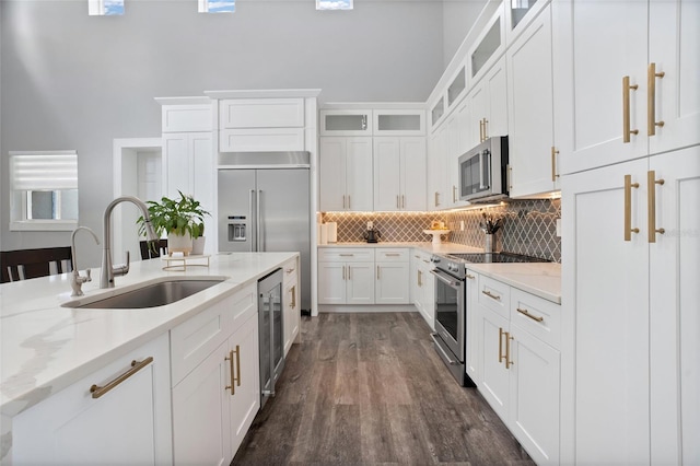 kitchen with dark wood-type flooring, stainless steel appliances, beverage cooler, light stone countertops, and sink