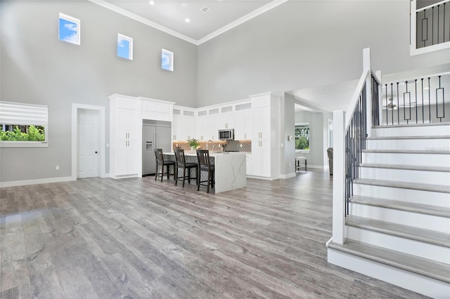 living room featuring a towering ceiling, light hardwood / wood-style flooring, ornamental molding, and plenty of natural light