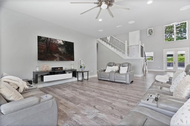 living room with ceiling fan, light hardwood / wood-style flooring, french doors, and a towering ceiling