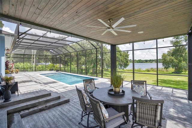 view of swimming pool with a lanai, ceiling fan, a water view, a patio area, and a lawn