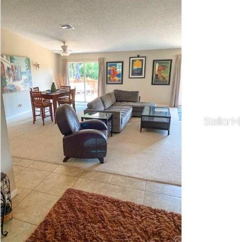 living room with a textured ceiling, light tile flooring, and ceiling fan