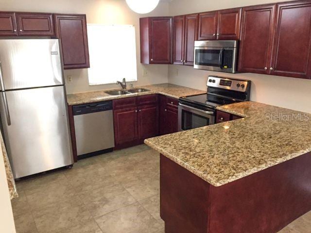 kitchen with light tile flooring, light stone countertops, kitchen peninsula, appliances with stainless steel finishes, and sink