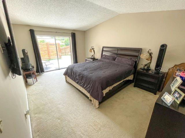 bedroom featuring light colored carpet, vaulted ceiling, access to outside, and a textured ceiling