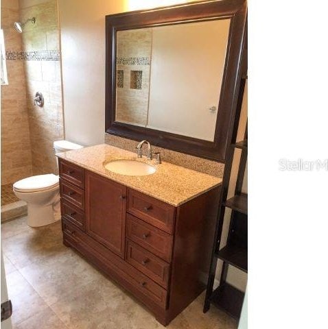 bathroom featuring toilet, a tile shower, large vanity, and tile flooring