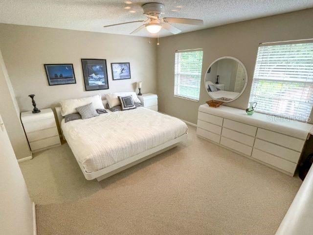 bedroom featuring light carpet, a textured ceiling, and ceiling fan