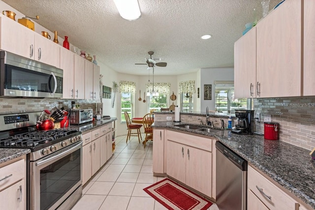 kitchen with light brown cabinets, tasteful backsplash, stainless steel appliances, and ceiling fan with notable chandelier