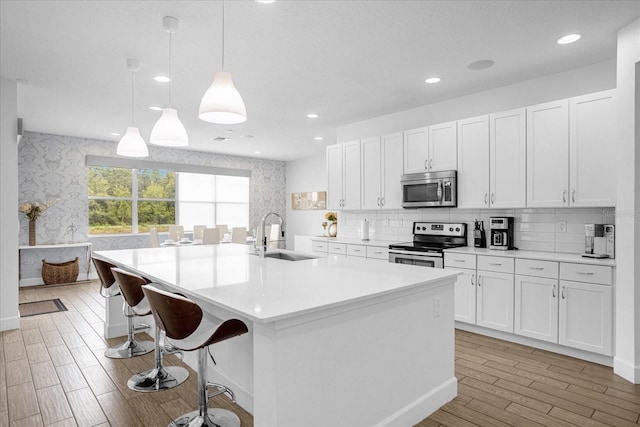 kitchen with sink, hanging light fixtures, a center island with sink, appliances with stainless steel finishes, and white cabinets