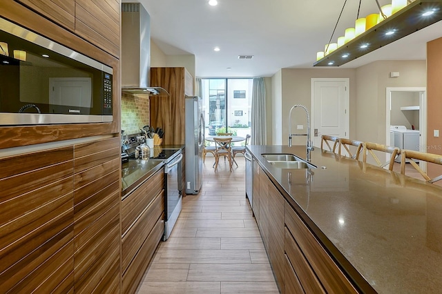 kitchen featuring hanging light fixtures, sink, stainless steel appliances, washer and clothes dryer, and wall chimney range hood