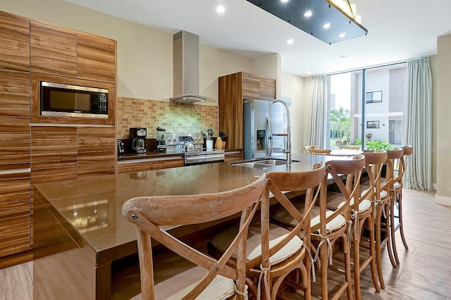 kitchen with wall chimney range hood, a kitchen breakfast bar, stainless steel appliances, and sink