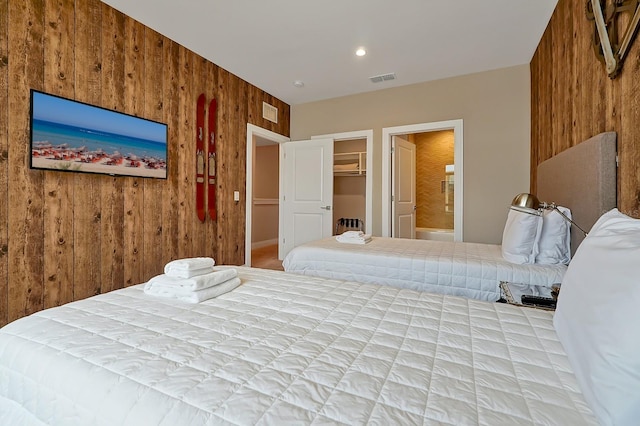 bedroom with a walk in closet, ensuite bathroom, a closet, and wood walls