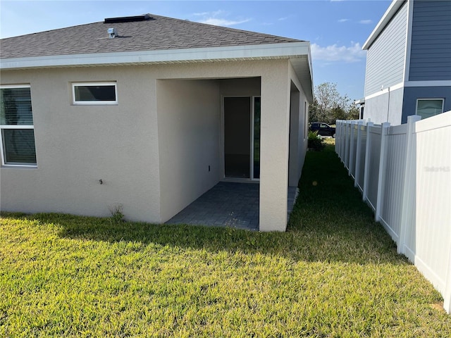 rear view of house with a yard, fence, roof with shingles, and stucco siding