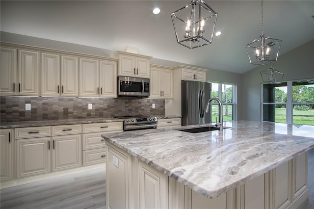 kitchen with tasteful backsplash, appliances with stainless steel finishes, hanging light fixtures, a kitchen island with sink, and light stone counters