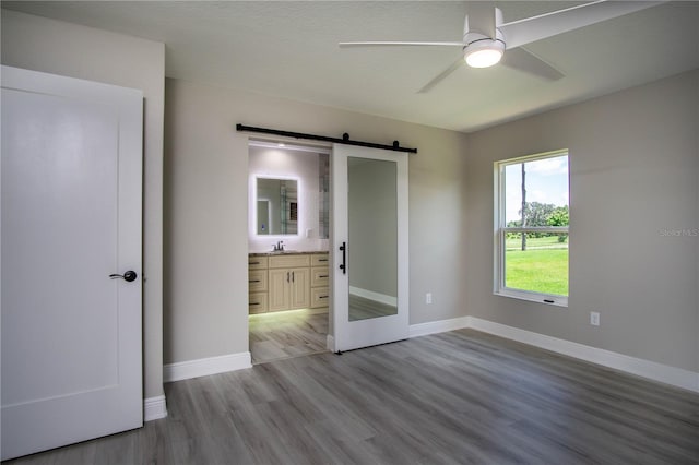 spare room featuring a barn door, sink, ceiling fan, and light wood-type flooring