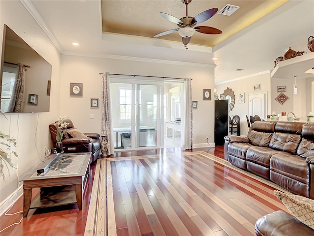 living room with ceiling fan, a raised ceiling, crown molding, and wood-type flooring