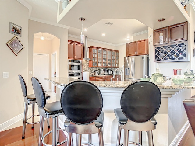 kitchen with light stone countertops, a kitchen breakfast bar, appliances with stainless steel finishes, decorative light fixtures, and tasteful backsplash