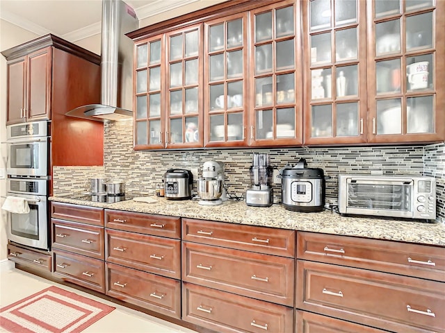 kitchen featuring wall chimney range hood, light stone countertops, tasteful backsplash, and double oven