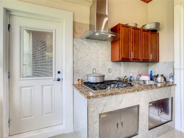 kitchen with backsplash, wall chimney range hood, light stone countertops, and stainless steel gas cooktop