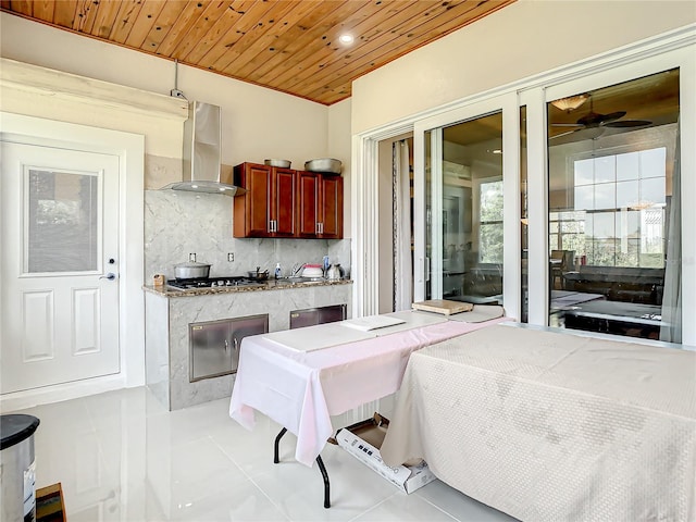 interior space with ceiling fan, tasteful backsplash, tile floors, wall chimney range hood, and wooden ceiling