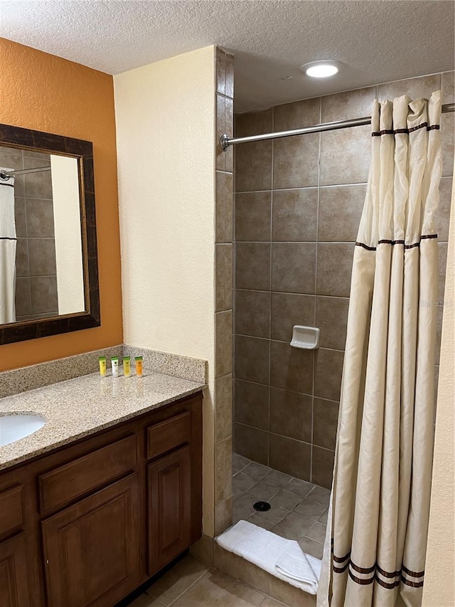 bathroom featuring tile patterned flooring, a textured ceiling, walk in shower, and vanity