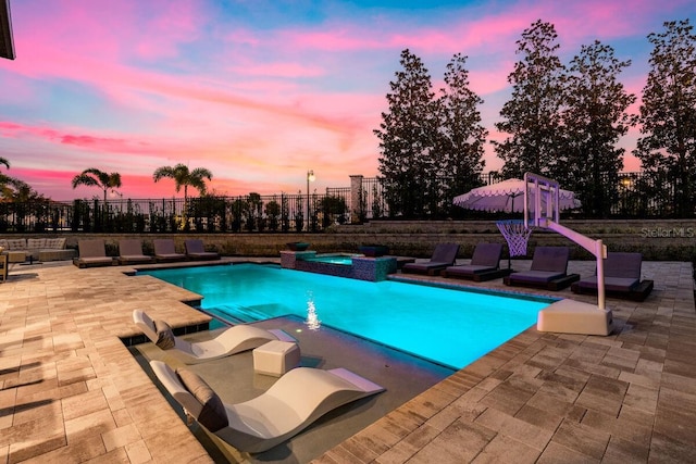 pool at dusk with an in ground hot tub and a patio area